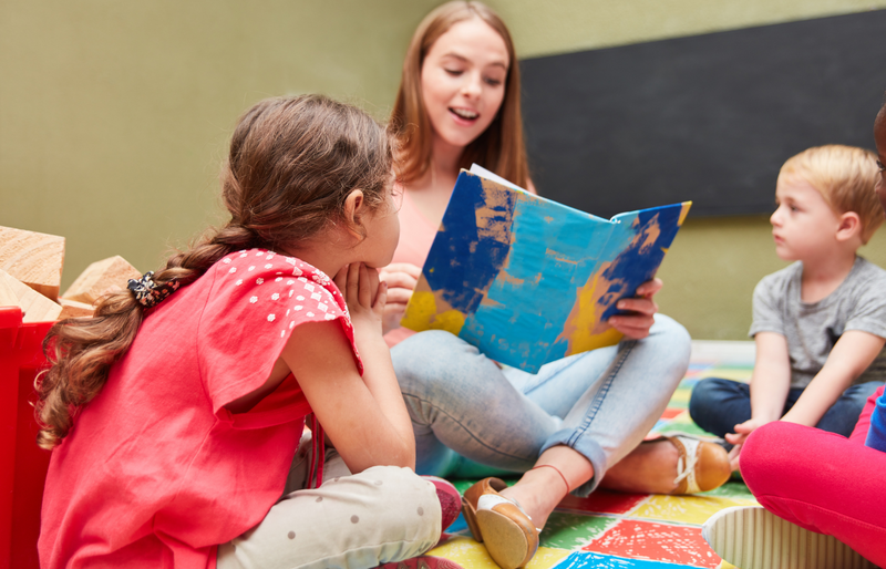 Frau liest zwei Kindern aus einem blauen Buch vor