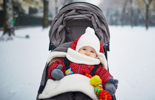 Ein Baby ist warm angezogen mit Mütze Schal und Handschuhen im Kinderwagen draußen im Schnee