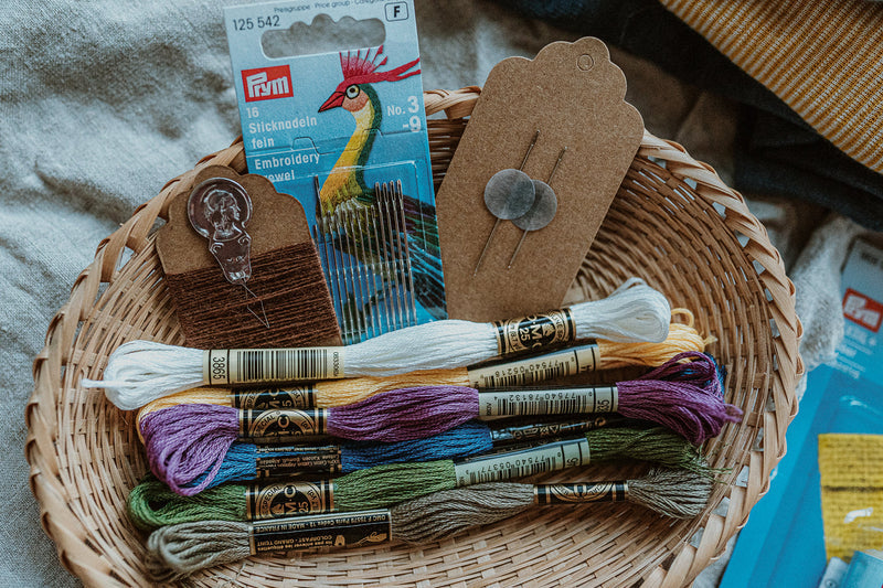 Kleiner Holzrahmen, Prym Textilkleber, DMC Baumwollgarn in verschiedenen Farben, feine Sticknadeln und 2 Webernadeln