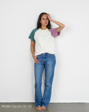 Eine Frau trägt ein weißes Raglan Shirt mit bunten Ärmeln der Marke Oktopulli im Unisex-Schnitt und lehnt an einer Wand