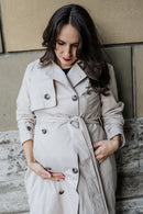 Frau trägt Trenchcoat und hält Babybauch