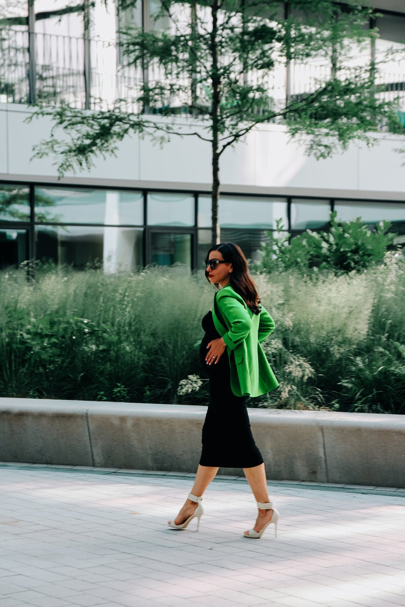 Frau mit grünem Umstandsblazer hält Babybauch