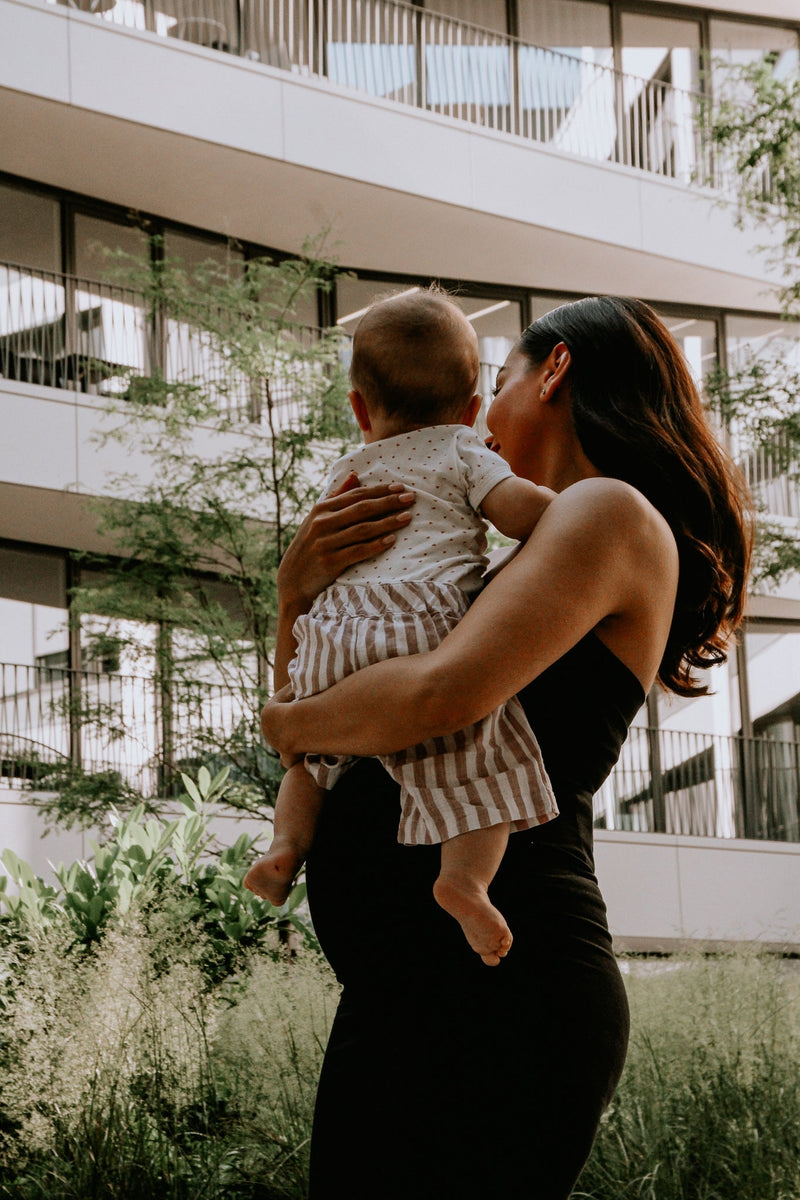 Schwangere Frau im schwarzen Umstandskleid mit Baby im Arm